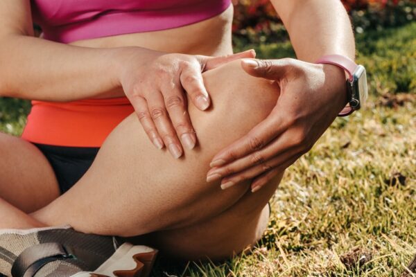 Close-up of a woman sitting cross-legged on grass, holding her knee, wearing a smartwatch.